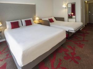 2 Betten in einem Hotelzimmer mit weißer Bettwäsche und roten Kissen in der Unterkunft Mercure Tours Nord in Tours