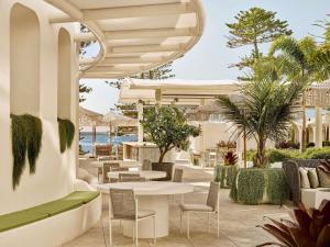 an outdoor patio with tables and chairs and palm trees at The Brighton Hotel Sydney - Mgallery Collection in Sydney