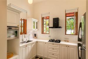 a kitchen with white cabinets and a sink and windows at La Dona by The Blue Kite - 4BHK Private Pool Villa in Assagao with Garden, Balcony, Caretaker & Spacious Living Area in Assagao