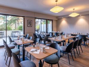 a restaurant with wooden tables and chairs and windows at Mercure Deauville Centre in Deauville