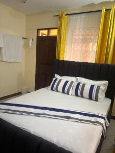 a bed with blue and white pillows and a window at AMTWAPA 2 bedroom pure blissful apartment ready to accommodate you and your family friends or colleagues in Mtwapa