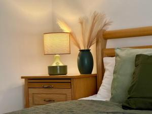 eine Vase auf einem Nachttisch mit einer Lampe auf einem Bett in der Unterkunft Cottage Apartman Gyula in Gyula