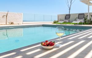 a glass of wine and a bowl of fruit next to a swimming pool at Awesome Home In Marina Di Ragusa in Marina di Ragusa