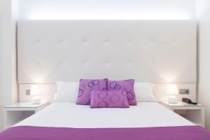 Una cama blanca con almohadas moradas encima. en Hotel Albahia Alicante, en Alicante