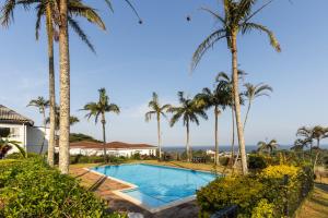 a pool with palm trees and the ocean in the background at The Notebook Hotel in Port Shepstone