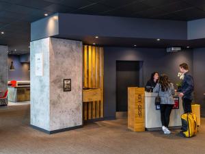 two people standing at a counter in a lobby at ibis Birmingham Airport Terminal Building - NEC in Bickenhill