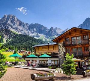 Un edificio de troncos con mesas y sombrillas y montañas. en Chalet Prà delle Nasse, en San Martino di Castrozza