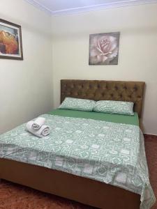 a bed with a green comforter and two towels at Ermal's House in Fier