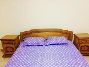 łóżko z fioletową pościelą i 2 drewnianymi stolikami nocnymi w obiekcie Apartmani Perić w Barze