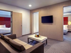 a living room with a couch and a tv on a wall at Grand Mercure Jakarta Harmoni in Jakarta +73 photos