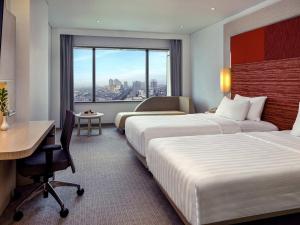 a hotel room with two beds and a desk and a window at Grand Mercure Jakarta Harmoni in Jakarta