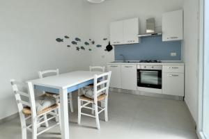 a white kitchen with a white table and chairs at Lèvè – Sea Nature Stay in Torre Lapillo