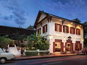a white house with red shutters on a street at 3 Nagas Hotel Luang Prabang - MGallery Collection in Luang Prabang