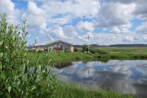 a house in a field with a reflection in the water at Grímsstaðir Guesthouse in Grímsstaðir á Fjöllum