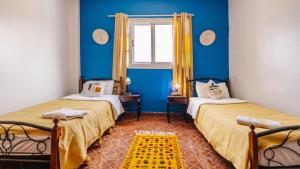 two beds in a room with blue walls and a window at Freebird Surfcamp Morocco in Agadir
