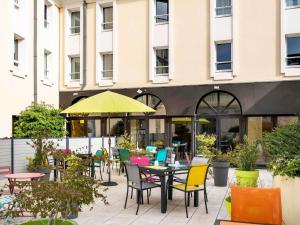 a patio with tables and chairs and a yellow umbrella at Mercure Trouville Sur Mer in Trouville-sur-Mer
