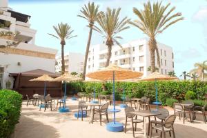 un patio avec tables et chaises avec parasols et palmiers dans l'établissement Intouriste Hôtel & Suites, à Agadir
