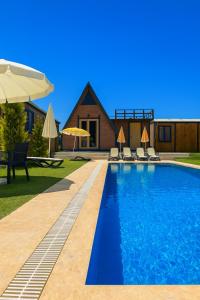 a pool with chairs and an umbrella and a house at La Bella Bungalov in Dosemealti