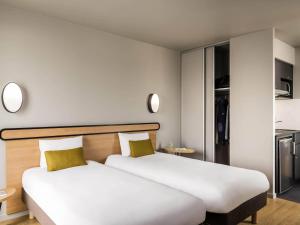 2 Betten in einem Hotelzimmer mit weißen und gelben Kissen in der Unterkunft Aparthotel Adagio access Colombes La Défense in Colombes + 34 Fotos