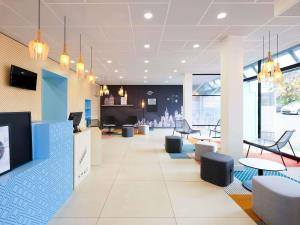 Un vestíbulo con sillas y mesas en un edificio. en Hôtel ibis Styles Auxerre Nord, en Auxerre