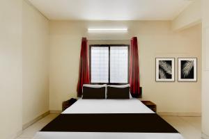 a bedroom with a bed and a window with red curtains at Hotel O Prarambh inn in Pune
