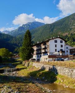 a building next to a river with mountains in the background at Villa Alpina Hotel in Forni di Sopra