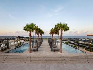 a pool with chairs and palm trees next to the ocean at Secrets Baby Beach Aruba Adults Only in Ceru Colorado