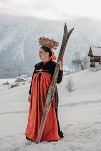 uma mulher de vestido vermelho segurando esquis na neve em Hotel Tradizio em Mittelberg