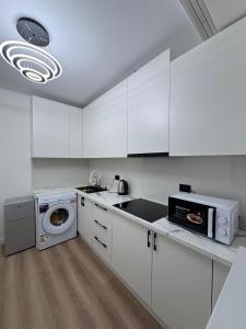 eine weiße Küche mit einer Waschmaschine und einer Mikrowelle in der Unterkunft Sunny Home Apartment in Almaty