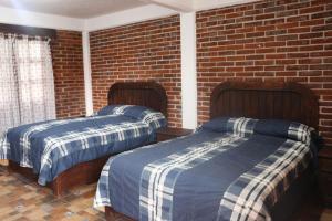 twee bedden in een kamer met een bakstenen muur bij Hotel Campestre El Rinconcito de Chigna in Chignahuapan
