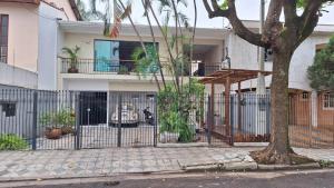 a white house with a fence and a tree at Pousada Lua Nova in Sorocaba