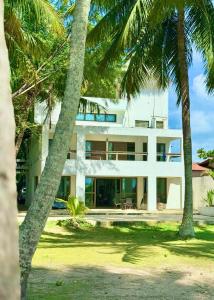 a white building with palm trees in front of it at Jardim Azul Praia in Pitimbu