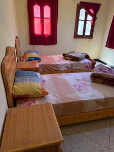 a room with two beds and two tables and windows at Auberge Ighounba in Tinerhir