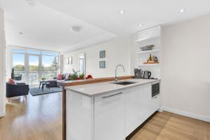 a white kitchen with a sink and a living room at Parkside at Waterfront in Downtown Calgary in Calgary