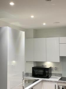 una cucina con mobili bianchi e un microonde nero di Posh 1 Bed Flat-Direct links to Central London a West Thurrock