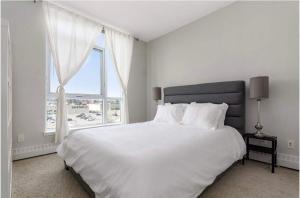 a white bedroom with a large bed with a large window at The Spruce Modern 2BR Condo with Pool & Parking in Calgary