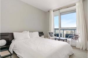 a bedroom with a white bed and a large window at The Spruce Modern 2BR Condo with Pool & Parking in Calgary