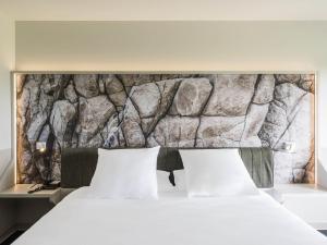 a bedroom with a stone wall above a bed at Mercure Hotel & Spa Bastia Biguglia in Biguglia