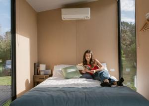 Una donna seduta su un letto che legge un libro di Golden Valley Retreat by Tiny Away a Waihi