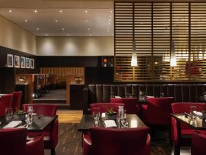 a dining room with tables and red chairs at Mövenpick Hotel Frankfurt City Messe in Frankfurt/Main