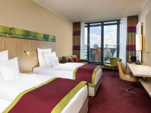 a hotel room with two beds and a desk at Mövenpick Hotel Frankfurt City Messe in Frankfurt/Main