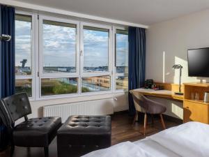 Una habitación de hotel con una cama, un escritorio y ventanas. en Mövenpick Hotel Nürnberg Airport, en Núremberg