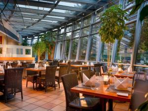 a restaurant with wooden tables and chairs and windows at Mövenpick Hotel München-Airport in Hallbergmoos