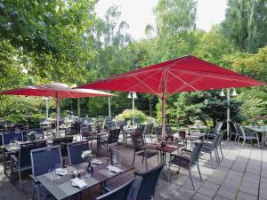 明斯特Mövenpick Hotel Münster am Aasee的一组带红色遮阳伞的桌椅