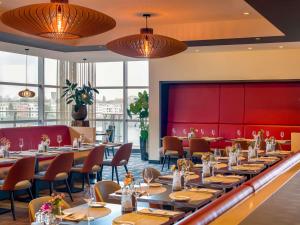 ein Restaurant mit Tischen und Stühlen und einer roten Wand in der Unterkunft Mövenpick Hotel Amsterdam City Centre in Amsterdam
