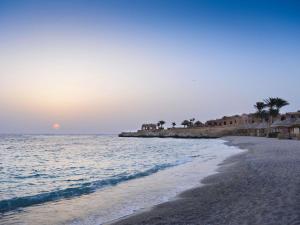 a beach with palm trees and the ocean at sunset at Movenpick Resort El Quseir in Quseir