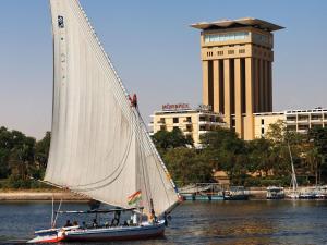 ein Segelboot im Wasser mit einem Gebäude im Hintergrund in der Unterkunft Mövenpick Resort Aswan in Assuan