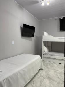 a white bedroom with a bed and a tv on the wall at Brisamar Suítes Ilha Grande in Angra dos Reis