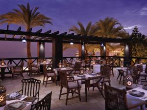Un restaurante con mesas y sillas y palmeras. en Mövenpick Resort & Residences Aqaba, en Áqaba