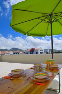 una mesa de madera con una sombrilla verde y platos en ella en Ocean Terrace House, en Ribeira Grande